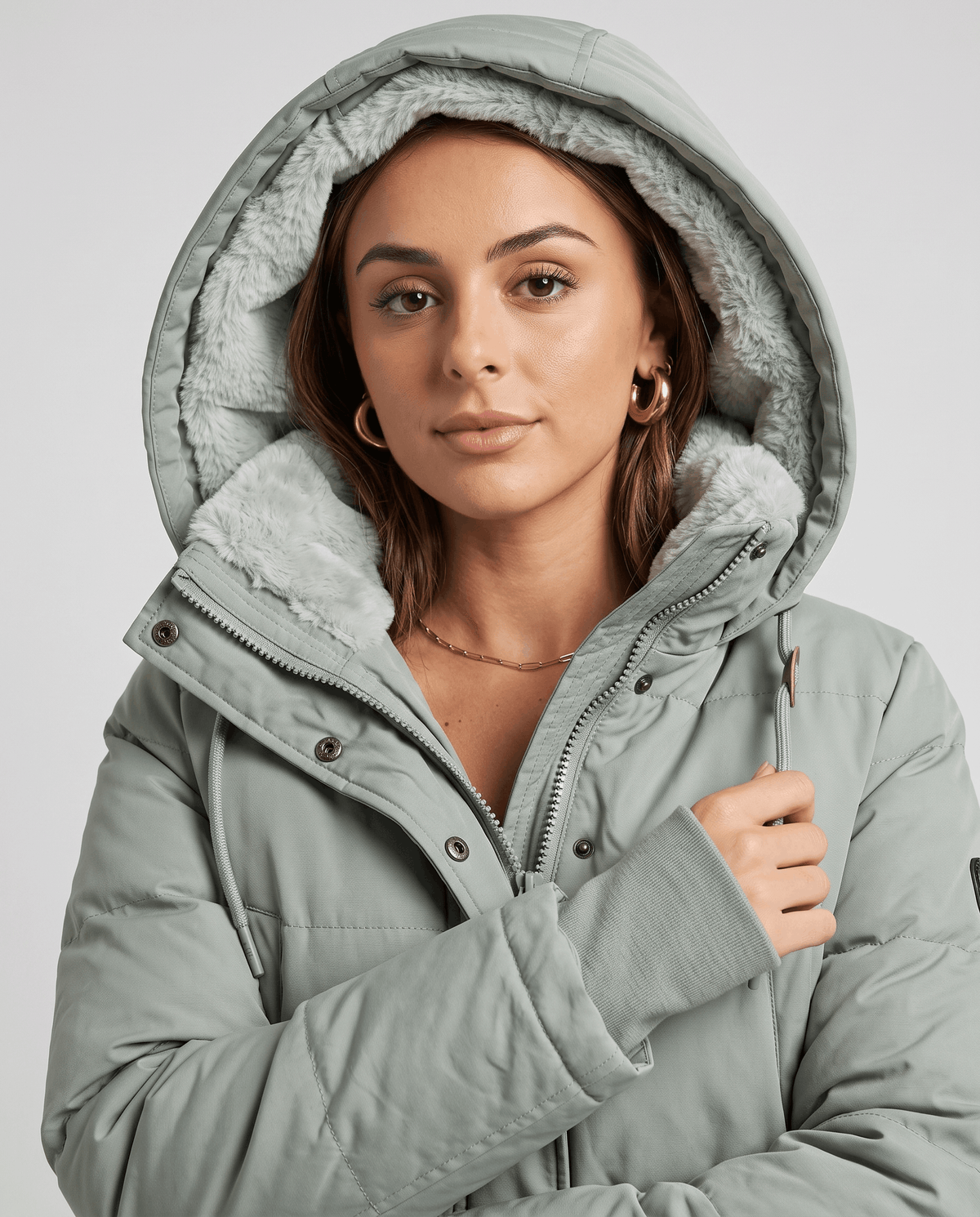 Model wearing the fleece-lined hood up on a sage green parka