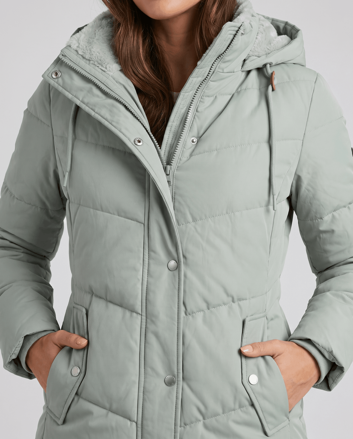 Hands in the side pockets of a sage green quilted parka