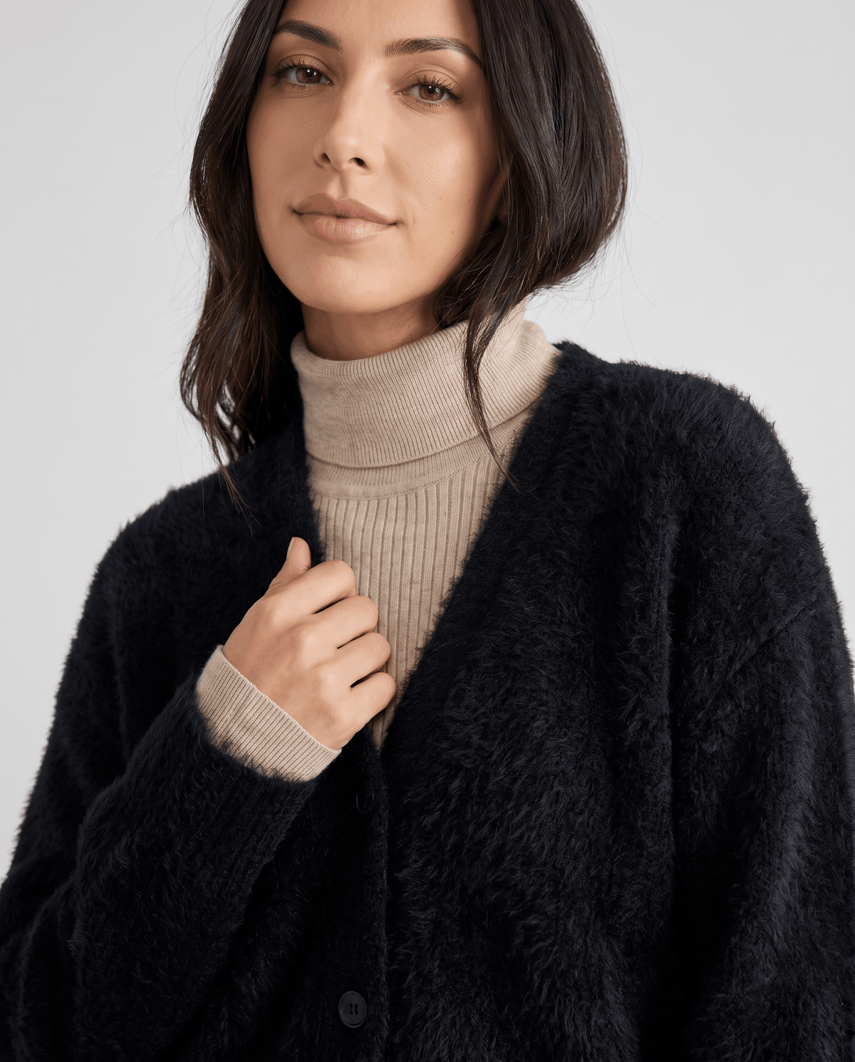 Black cardigan detail with a hand at the collar and front buttons