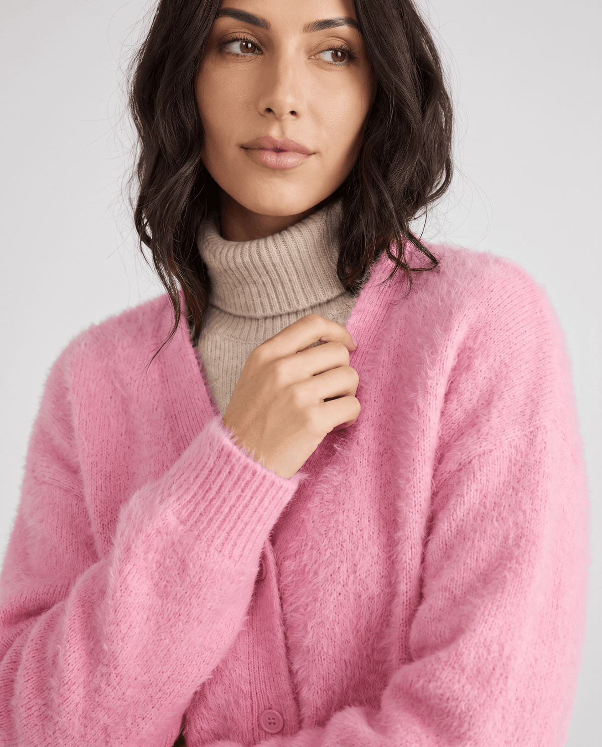 Pink cardigan close-up over a beige turtleneck with a hand at the collar