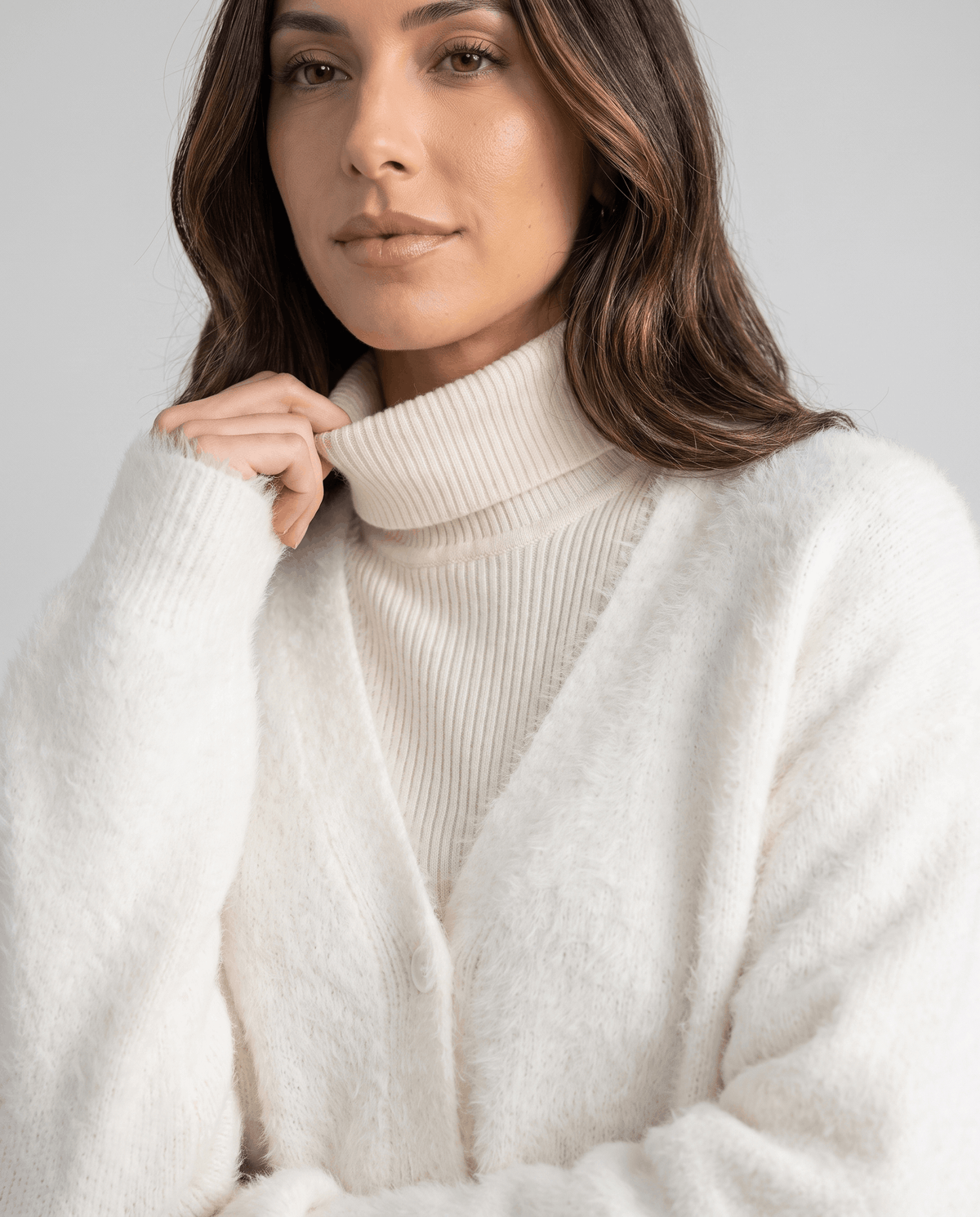 White cardigan close-up with a hand at the turtleneck collar