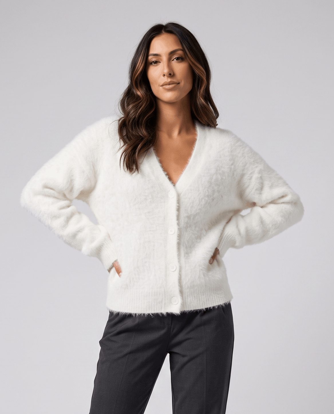 White cardigan with hands in pockets and charcoal trousers
