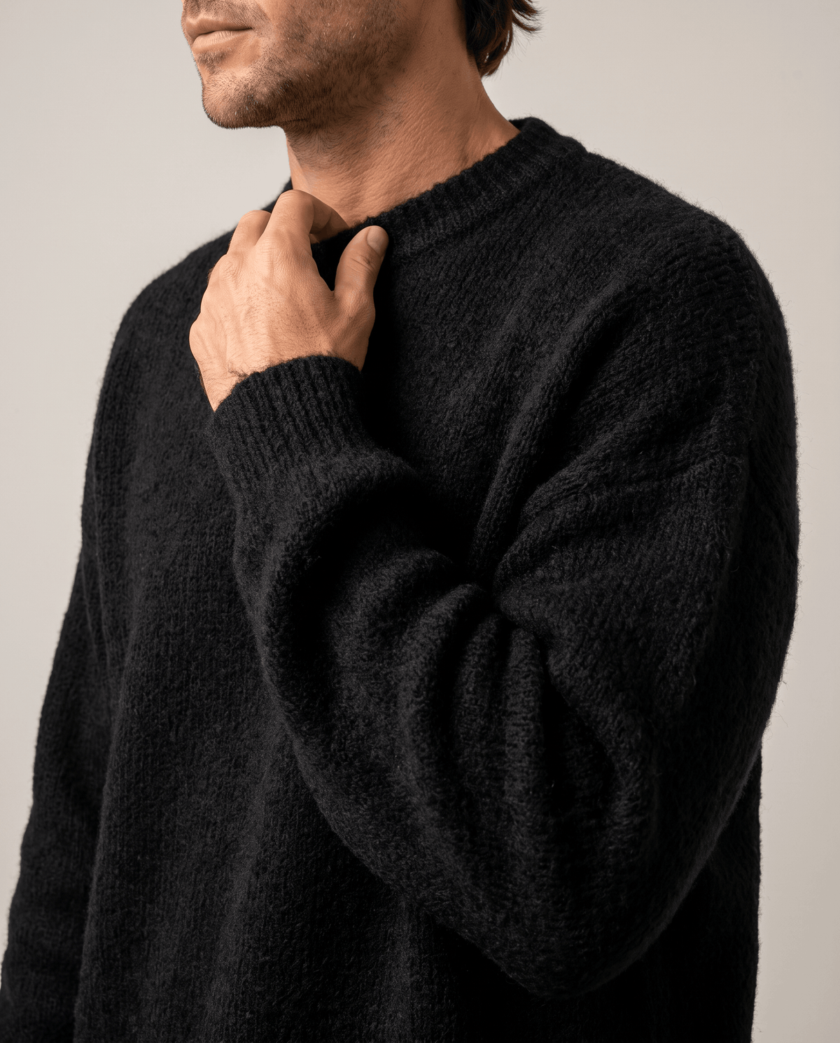 Close-up of a hand at the ribbed crew neck of the black fuzzy sweater