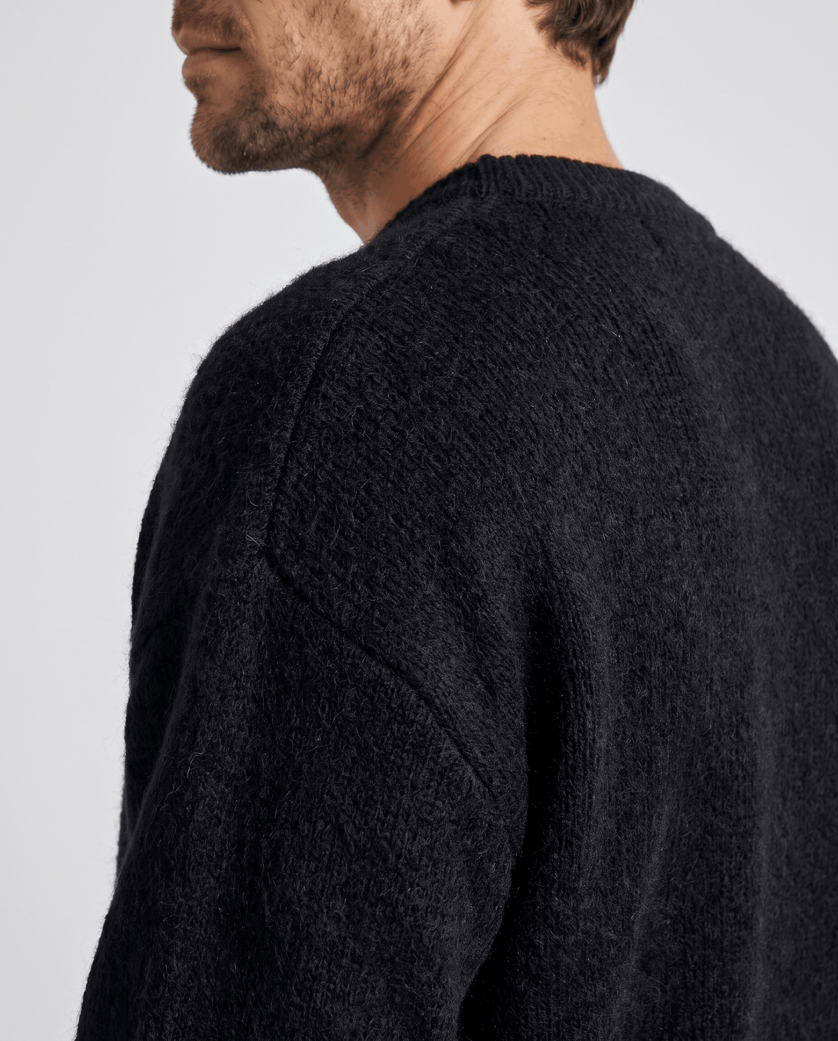 Shoulder detail of the black knit pullover showing its soft brushed texture