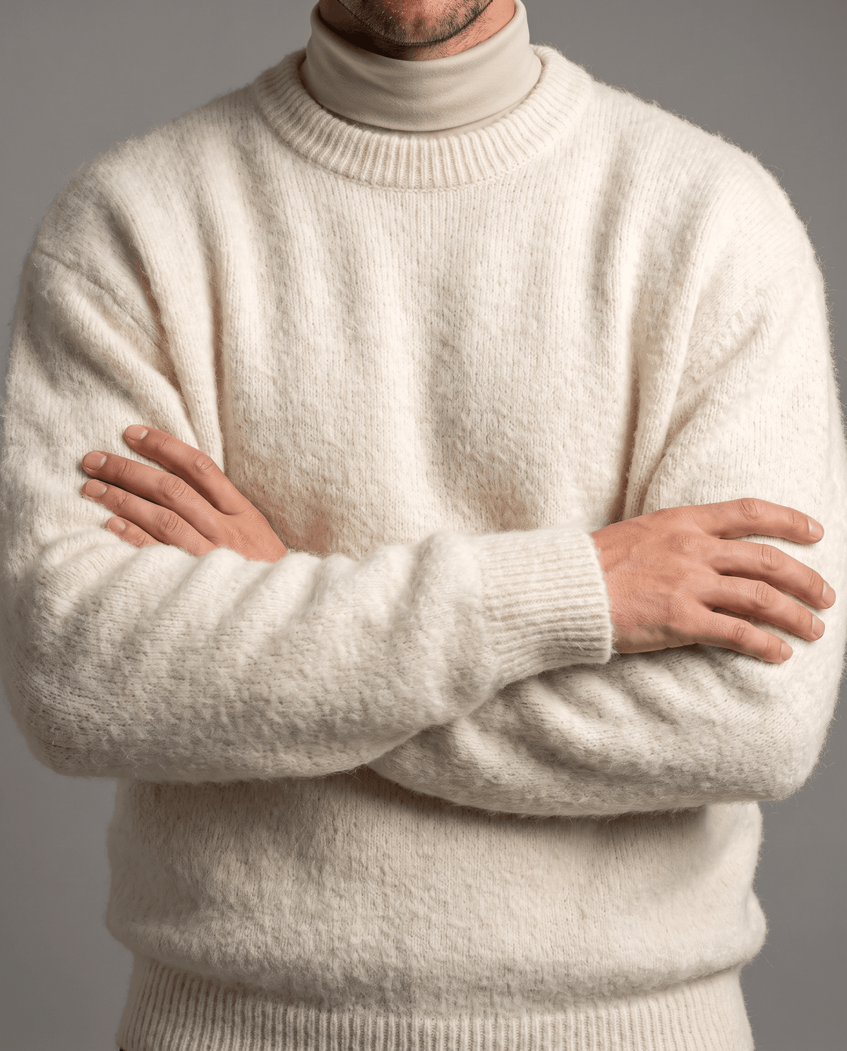 Front close-up of the white knit sweater worn over a cream turtleneck, arms crossed