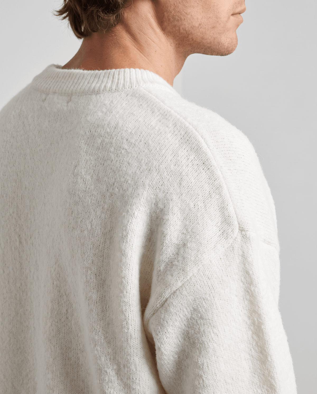Back shoulder detail of the white sweater showing the soft knit and dropped seam