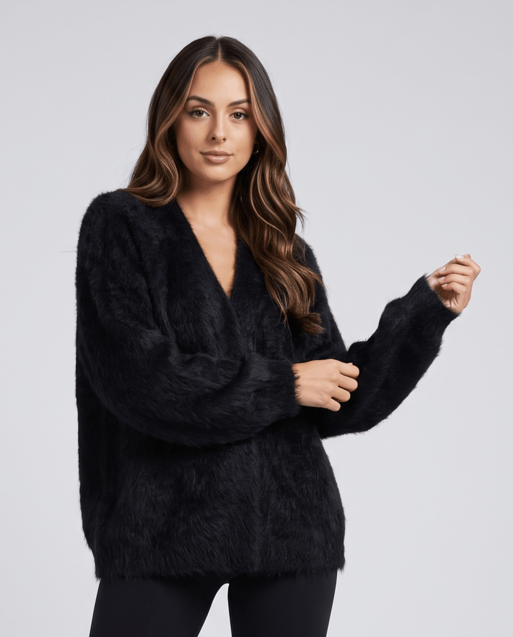 Black cardigan front view with one hand raised and slim black pants