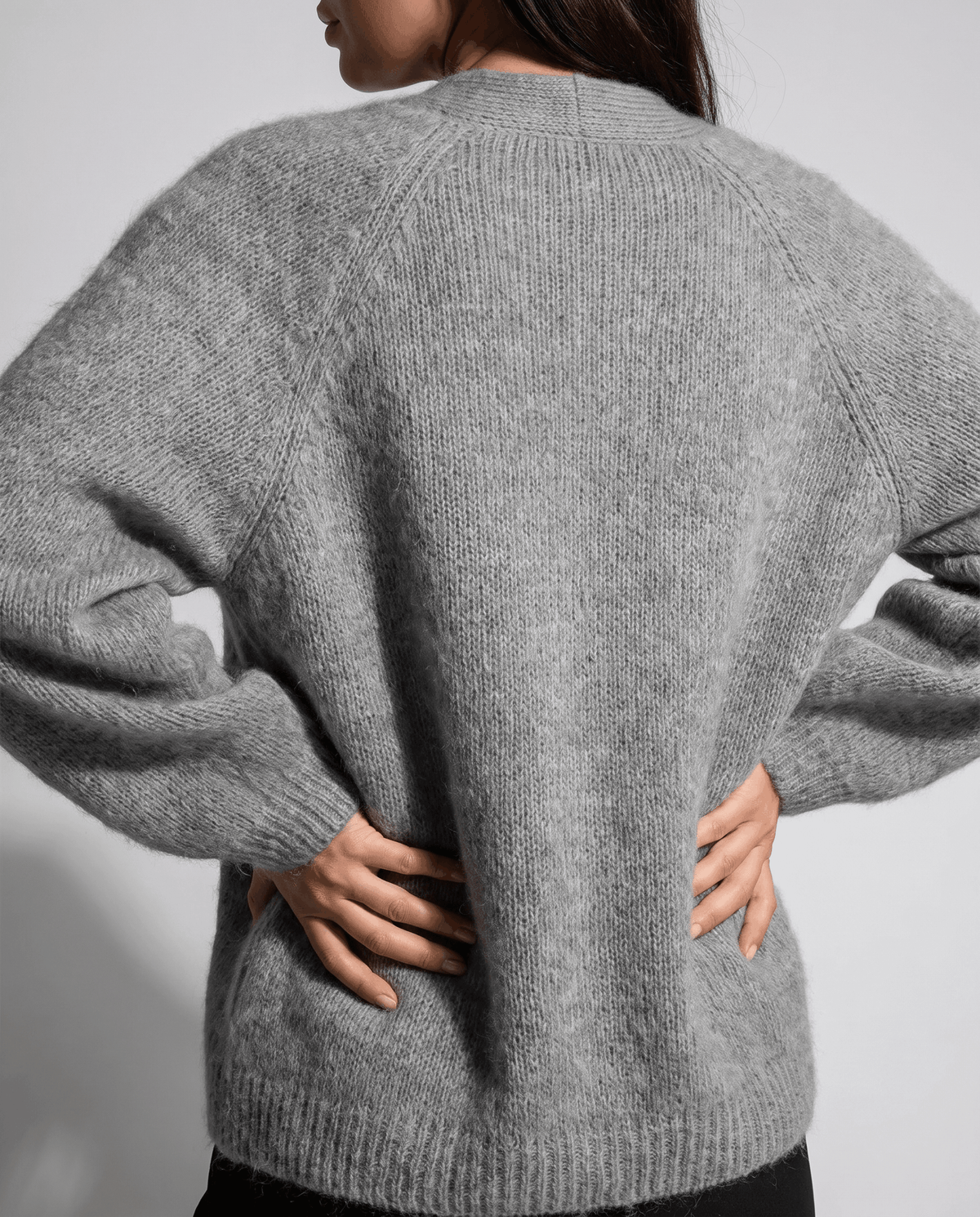 Back view of the gray cardigan with hands on hips and ribbed hem visible