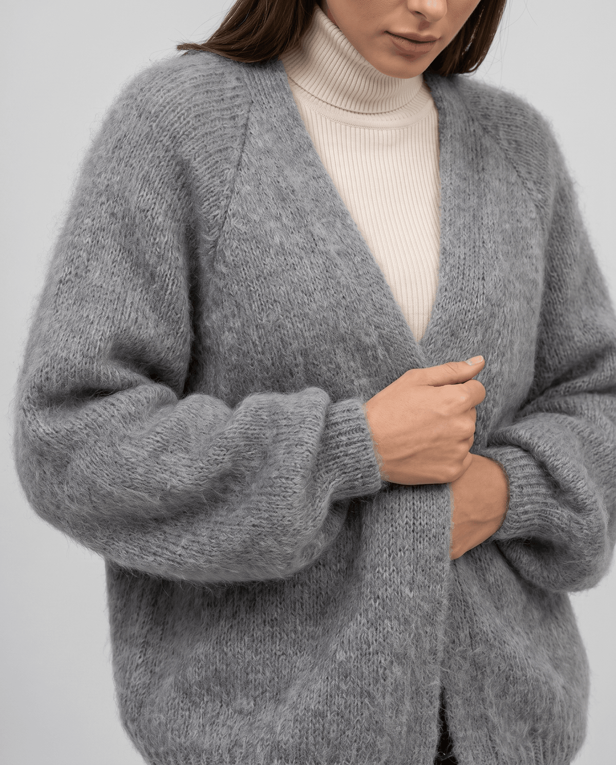 Close-up of the gray cardigan held closed over a cream turtleneck sweater