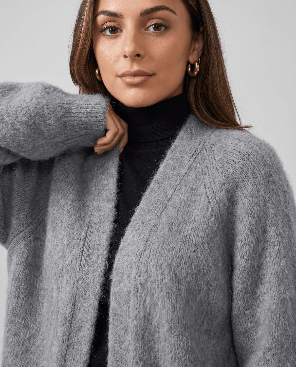 Gray cardigan over a black turtleneck with a hand at the collar