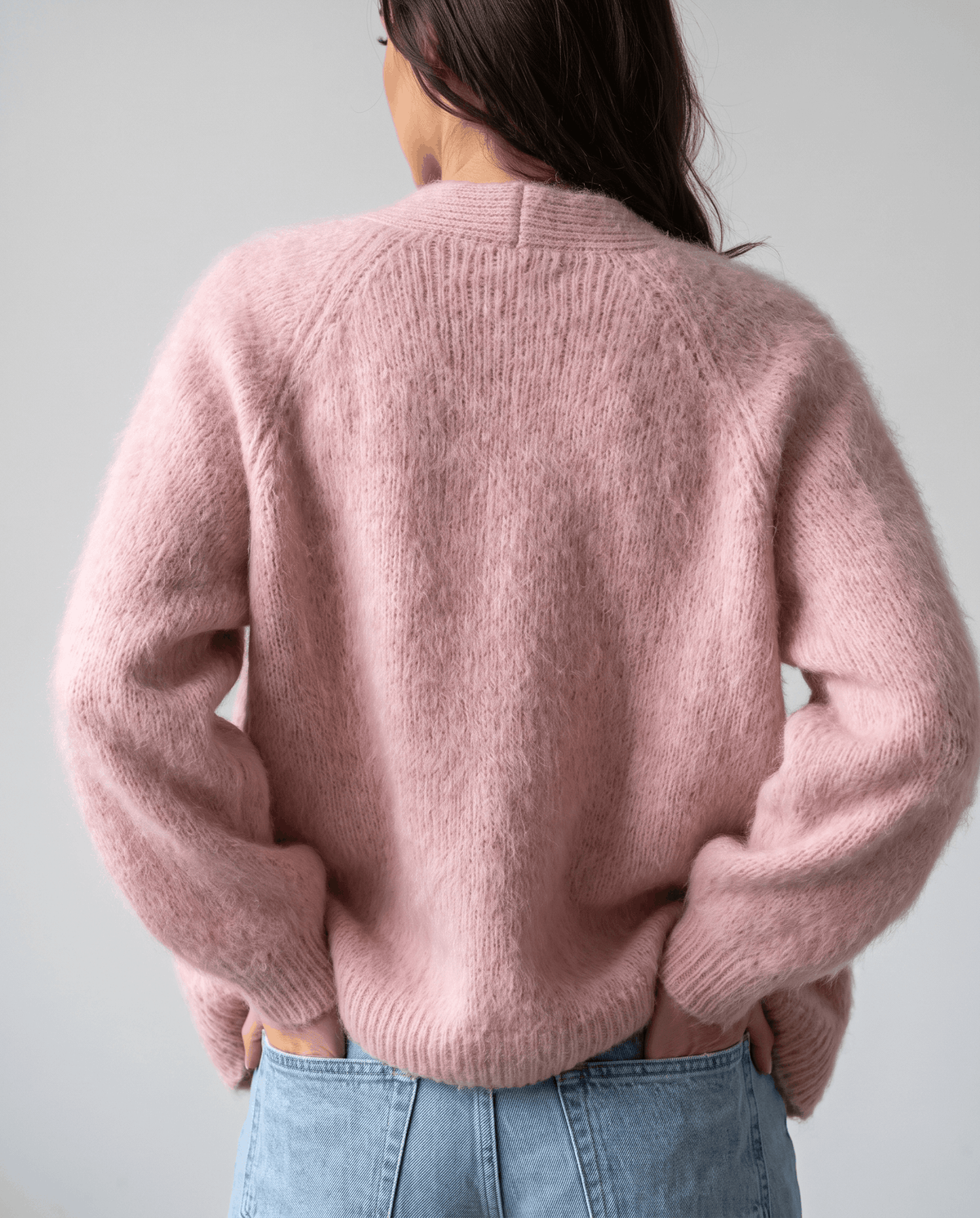 Back view of the pink cardigan with ribbed hem worn over light blue jeans