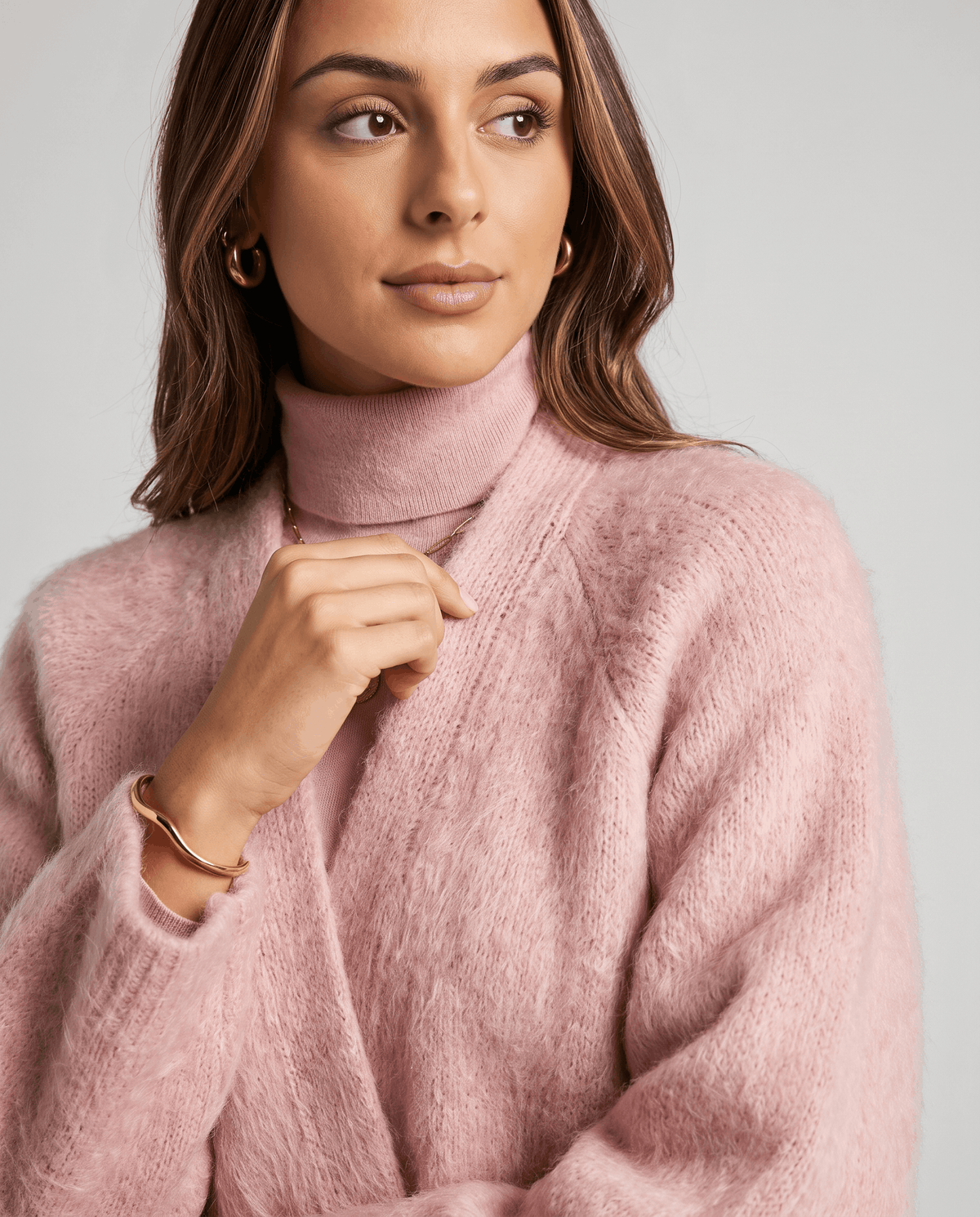 Pink cardigan worn over a pink turtleneck with a hand resting at the open front