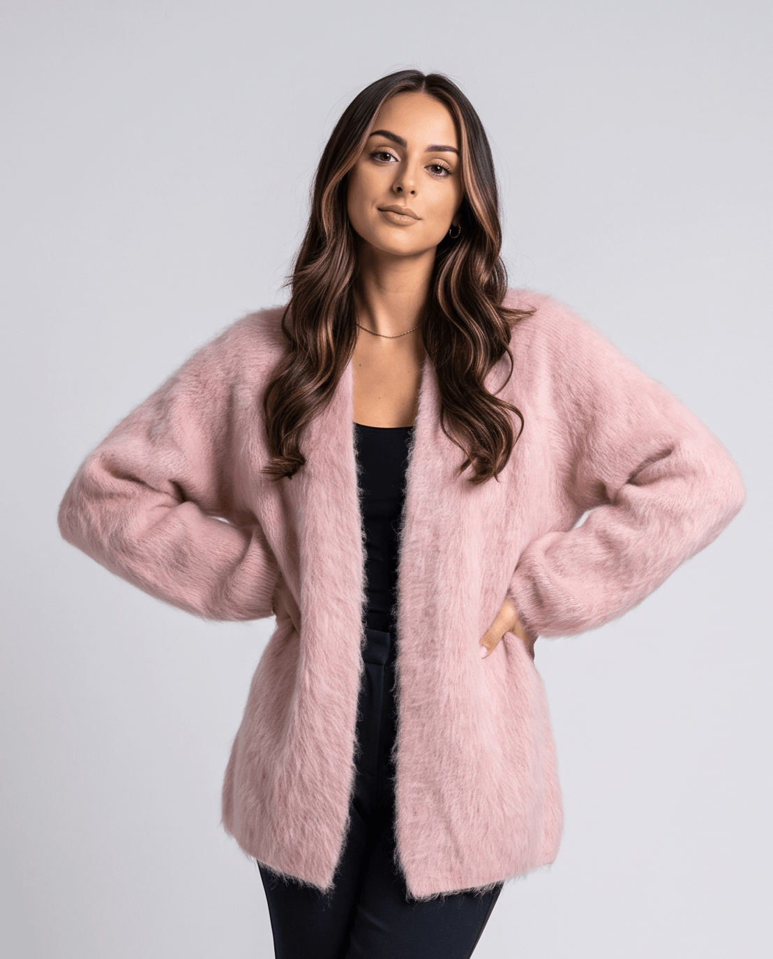 Women's fuzzy open-front cardigan in pink over a black top with hands on hips