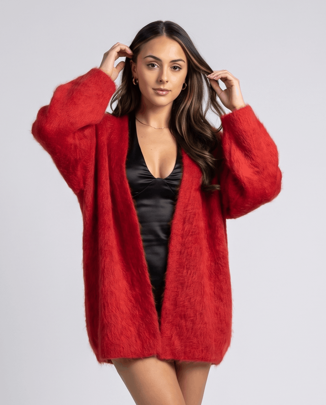 Red cardigan over a black satin slip with both hands lifting the hair