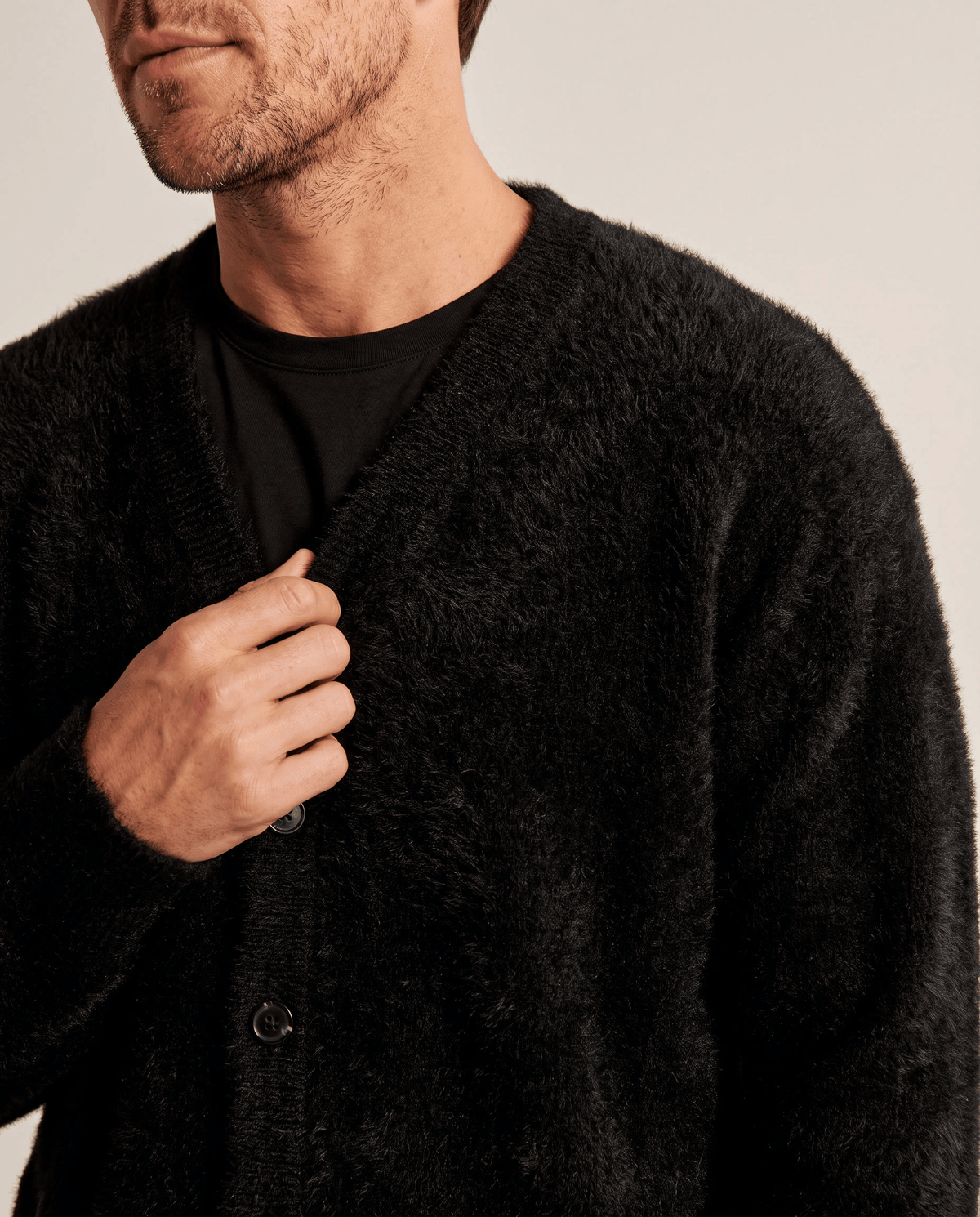 Close-up of a hand on the button placket of the black knit cardigan