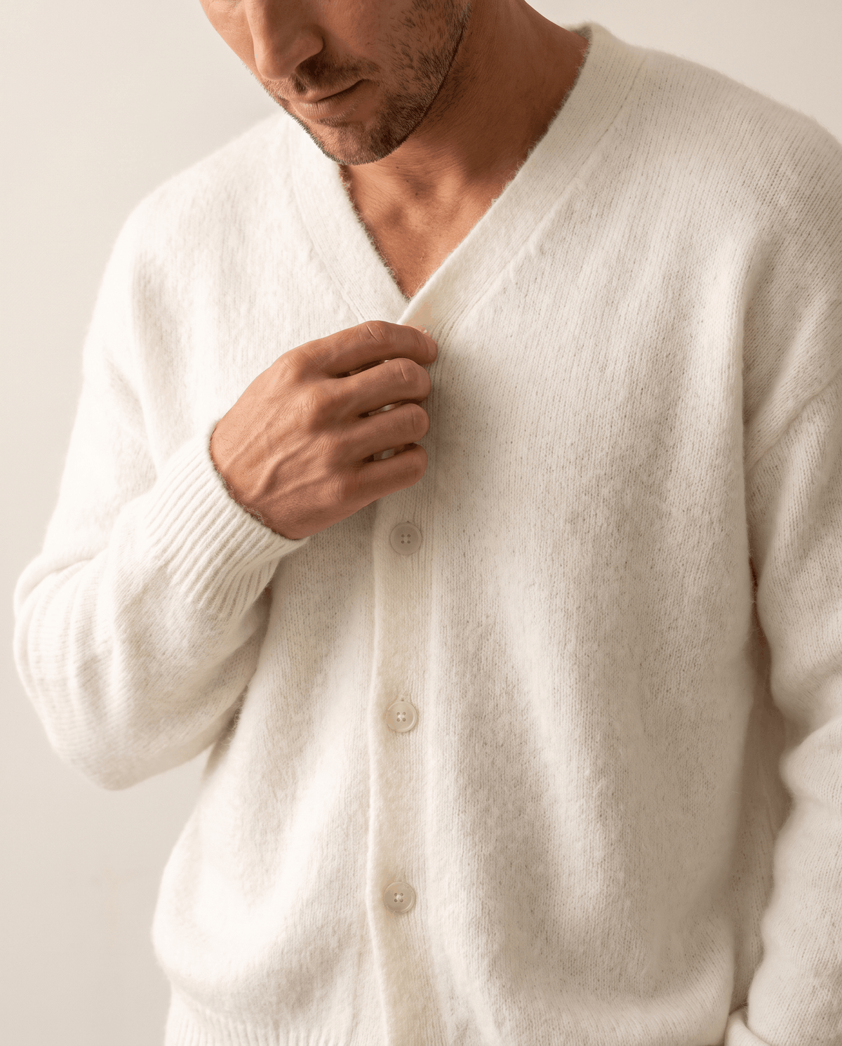 Hand resting on the V-neck and buttons of the white brushed knit cardigan