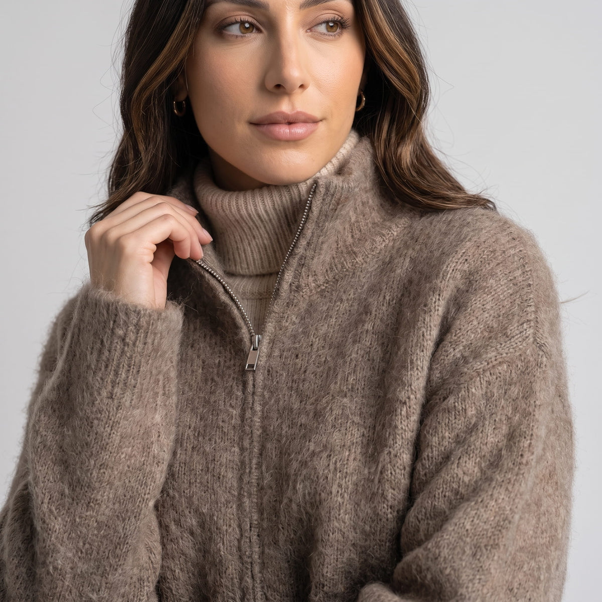Model pulling the zip at the stand collar, layered over a taupe turtleneck sweater