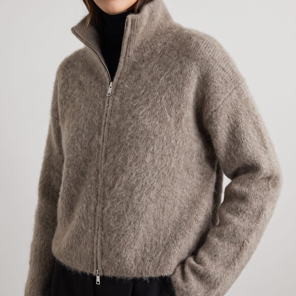 Front close-up of the zipped taupe knit cardigan with stand collar over a black turtleneck