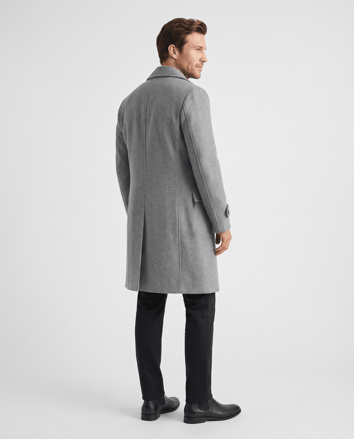 Back view of a long gray wool coat worn with black trousers and boots
