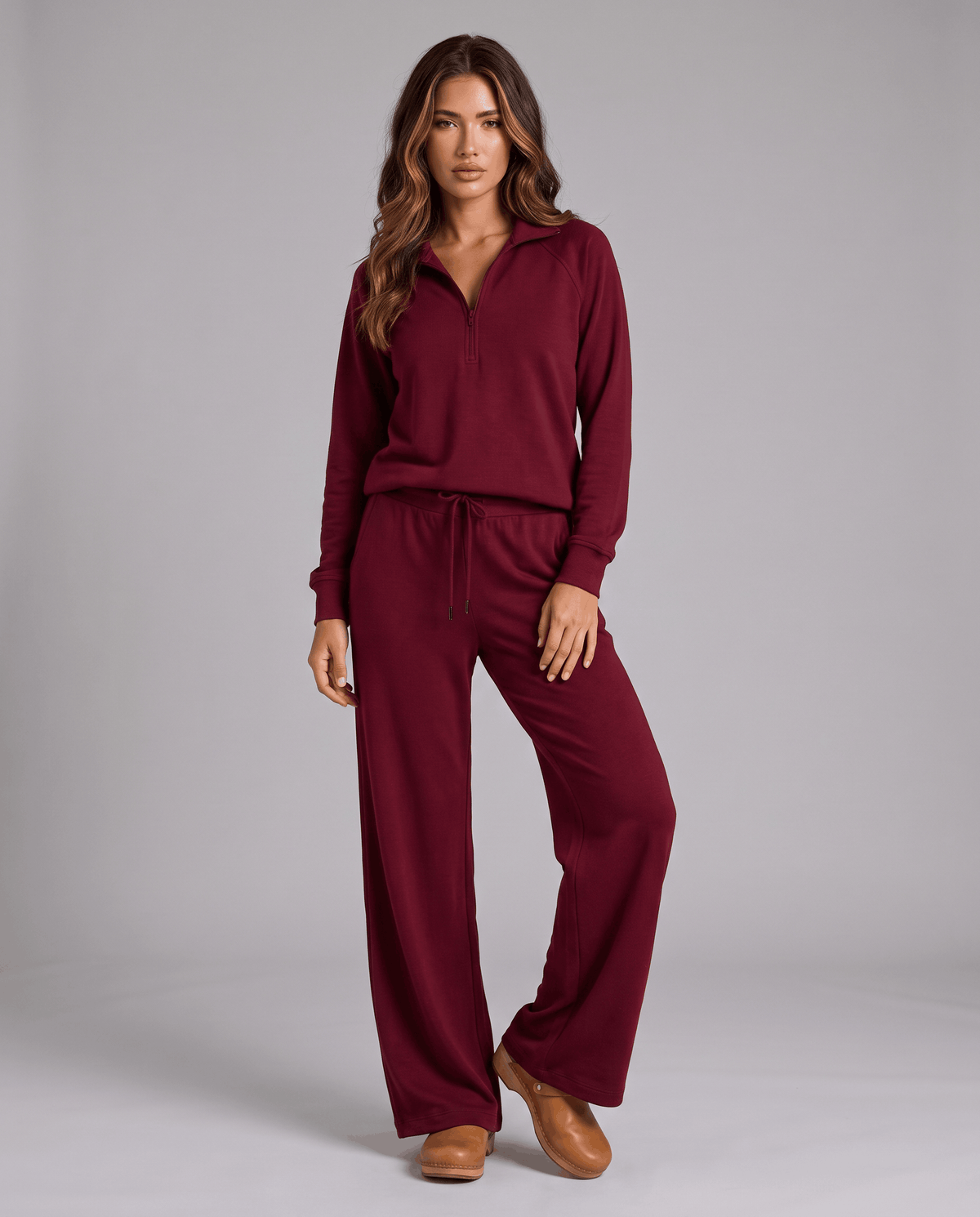 Woman in burgundy half-zip top and wide-leg pants standing in a studio