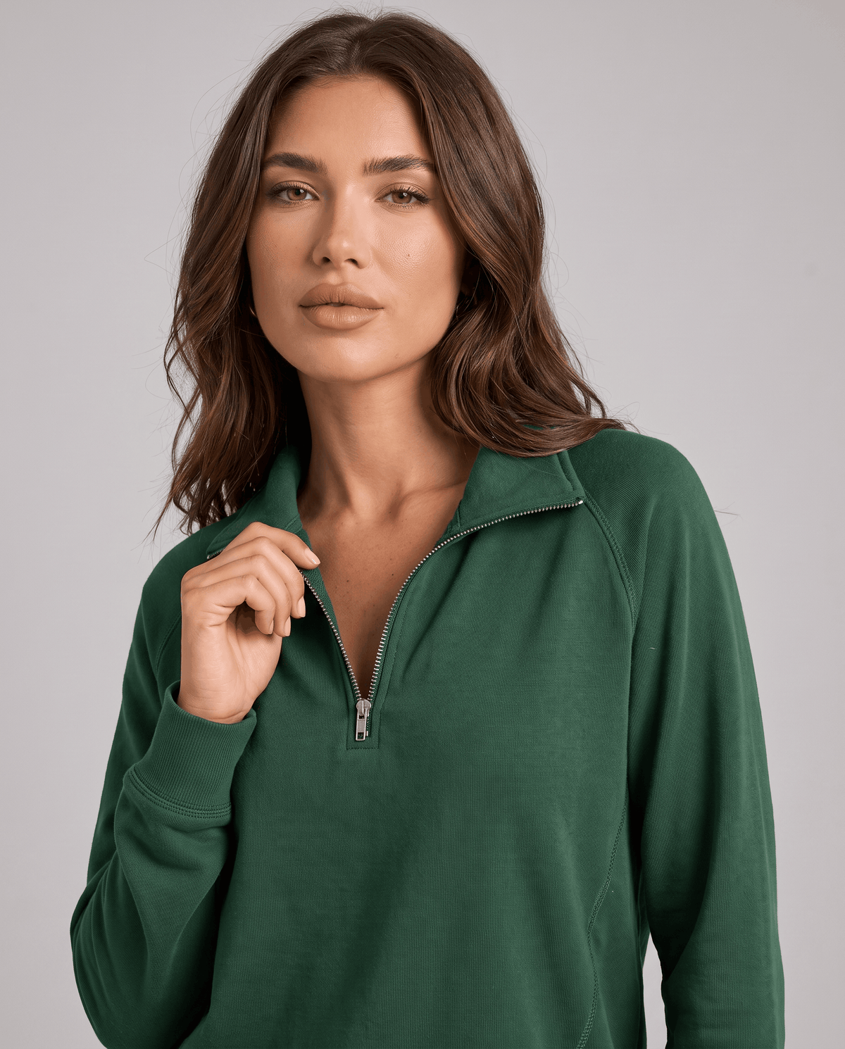 Close-up of green half-zip collar and raglan sleeve on a model touching the zip