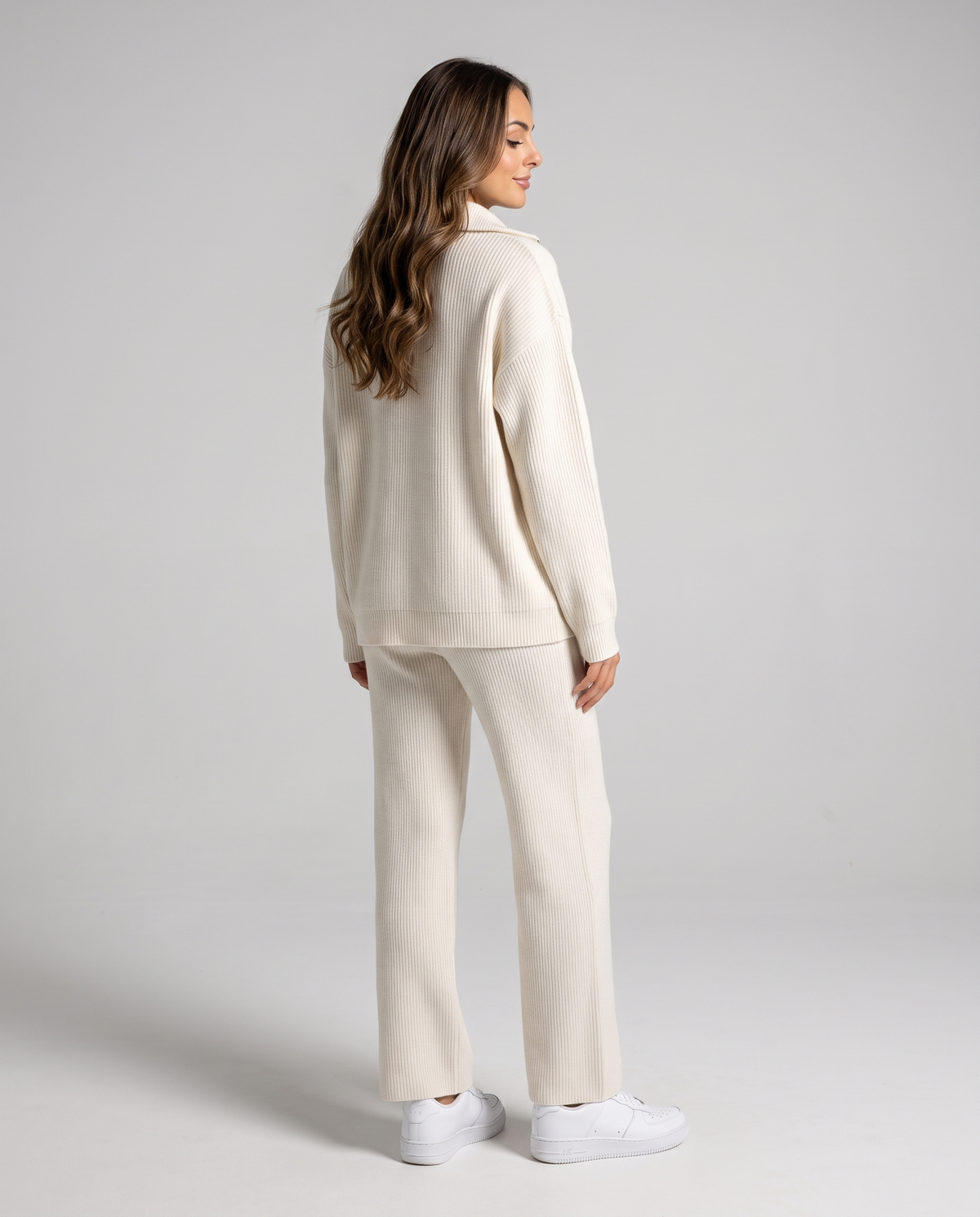 Back view of the beige knit pullover with a folded collar, worn with matching pants