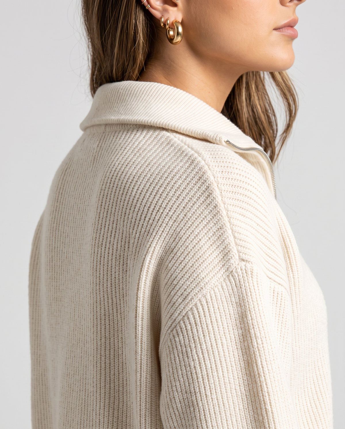 Side close-up of the folded collar and ribbed sleeve on the beige knit pullover