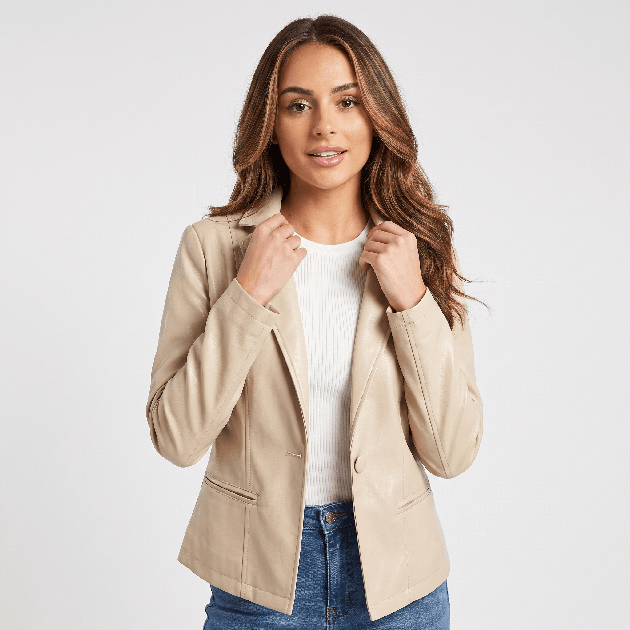 Woman wearing a beige faux leather blazer with a notched lapel, single-button closure, front flap pockets, and a tailored fit over a white top and blue jeans.