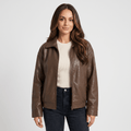 Woman wearing a brown faux leather jacket with a zip-front closure, classic collar, and straight-fit silhouette over a cream top and dark jeans.