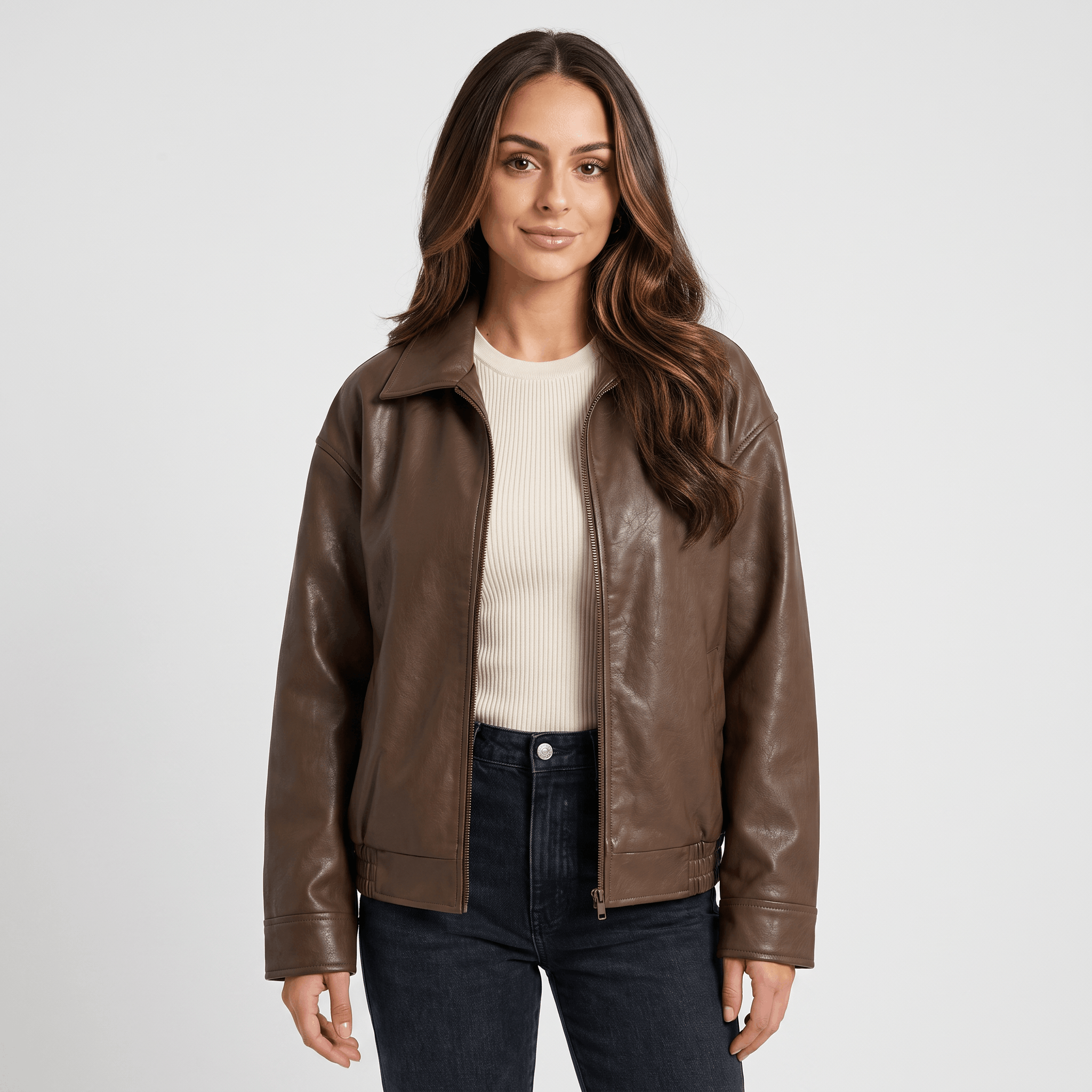 Woman wearing a brown faux leather jacket with a zip-front closure, classic collar, and straight-fit silhouette over a cream top and dark jeans.