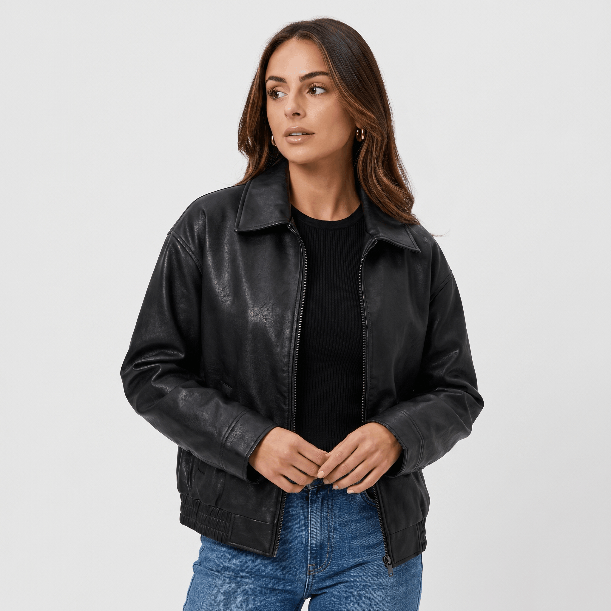 Woman wearing a black faux leather jacket with a zip-front closure, classic collar, and relaxed fit over a black top and dark jeans.
