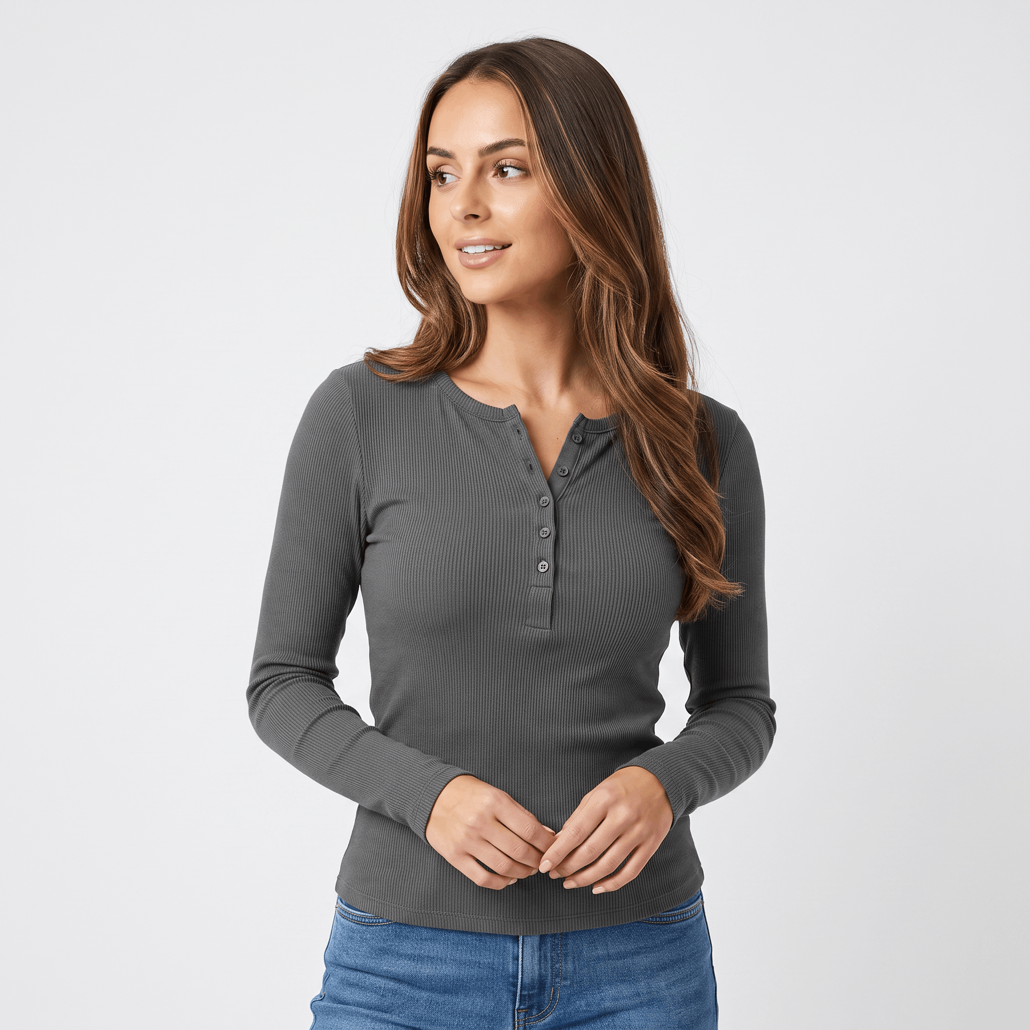 Woman wearing a gray ribbed henley top with a button neckline, long sleeves, fitted silhouette, and blue jeans.