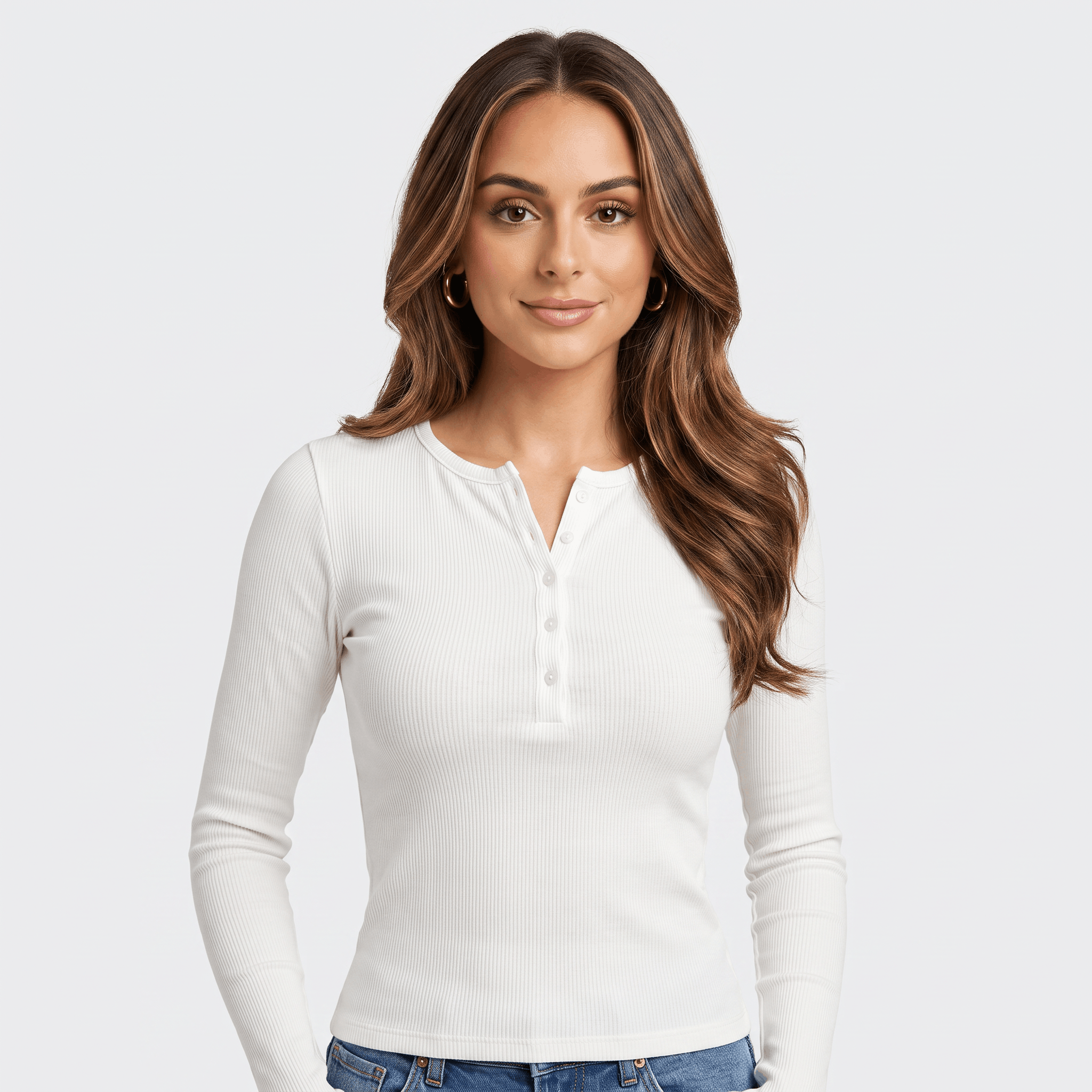 Woman wearing a white long sleeve ribbed henley top with a button neckline and fitted silhouette paired with blue jeans.
