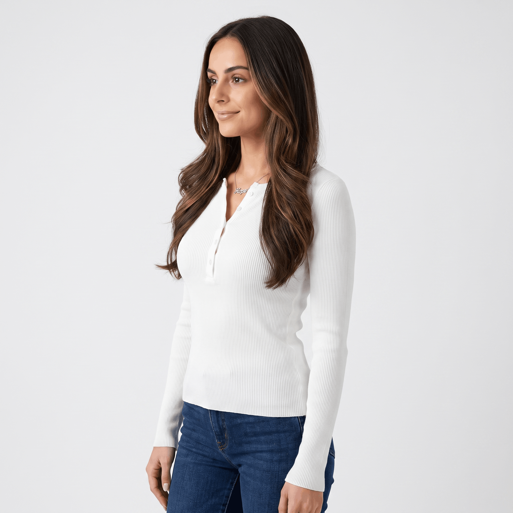 Side view of a woman wearing a white ribbed henley top with a fitted silhouette, long sleeves, and buttoned neckline.