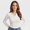 Woman wearing a white ribbed henley top with a buttoned neckline, long sleeves, fitted silhouette, and textured knit fabric with blue jeans.