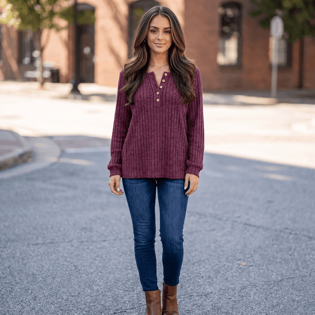 Woman wearing a burgundy textured henley sweater with blue jeans while walking along a city street.
