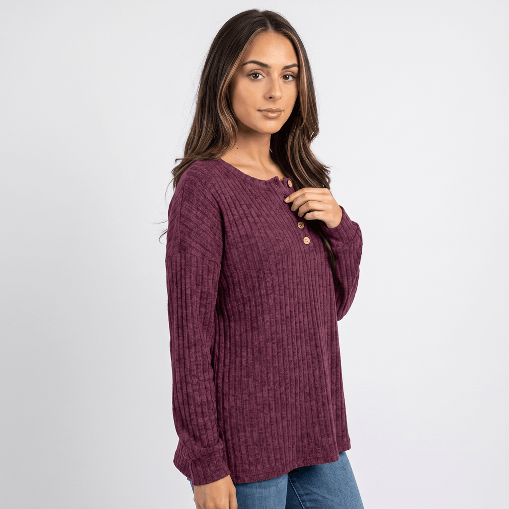 Side view of a woman wearing a burgundy textured henley sweater with a button neckline and long sleeves.