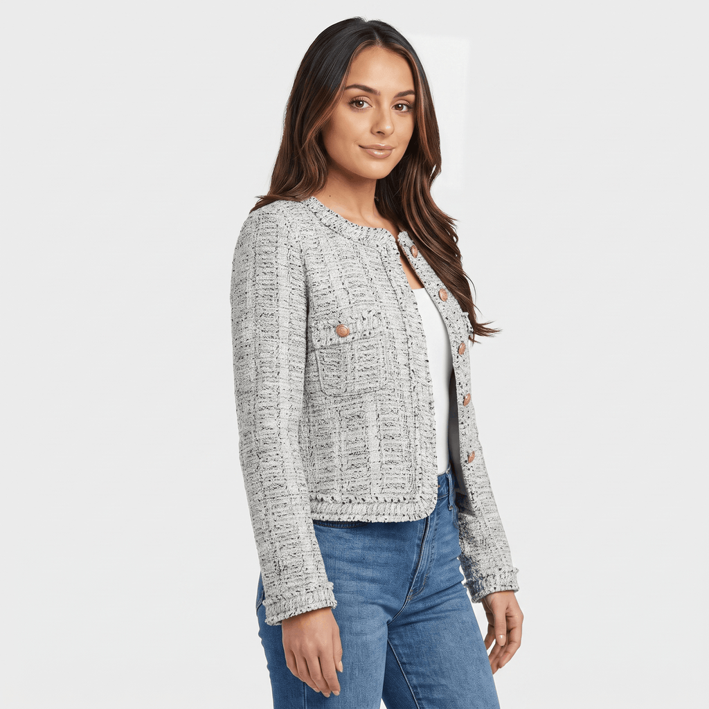 Side view of a woman wearing a light gray textured tweed jacket with gold-tone buttons, round neckline, and tailored fit with blue jeans.