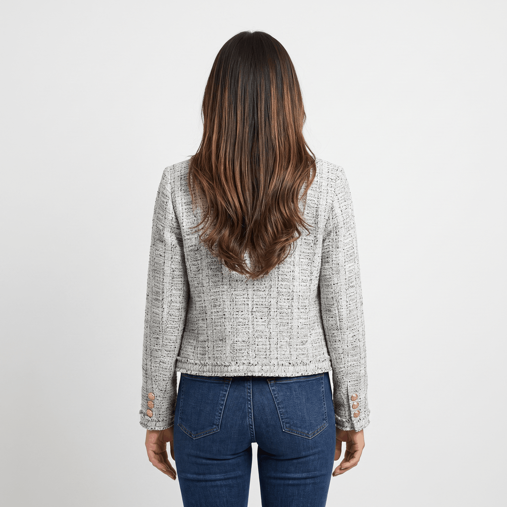 Back view of a woman wearing a light gray textured tweed jacket with a tailored cropped fit and long sleeves.