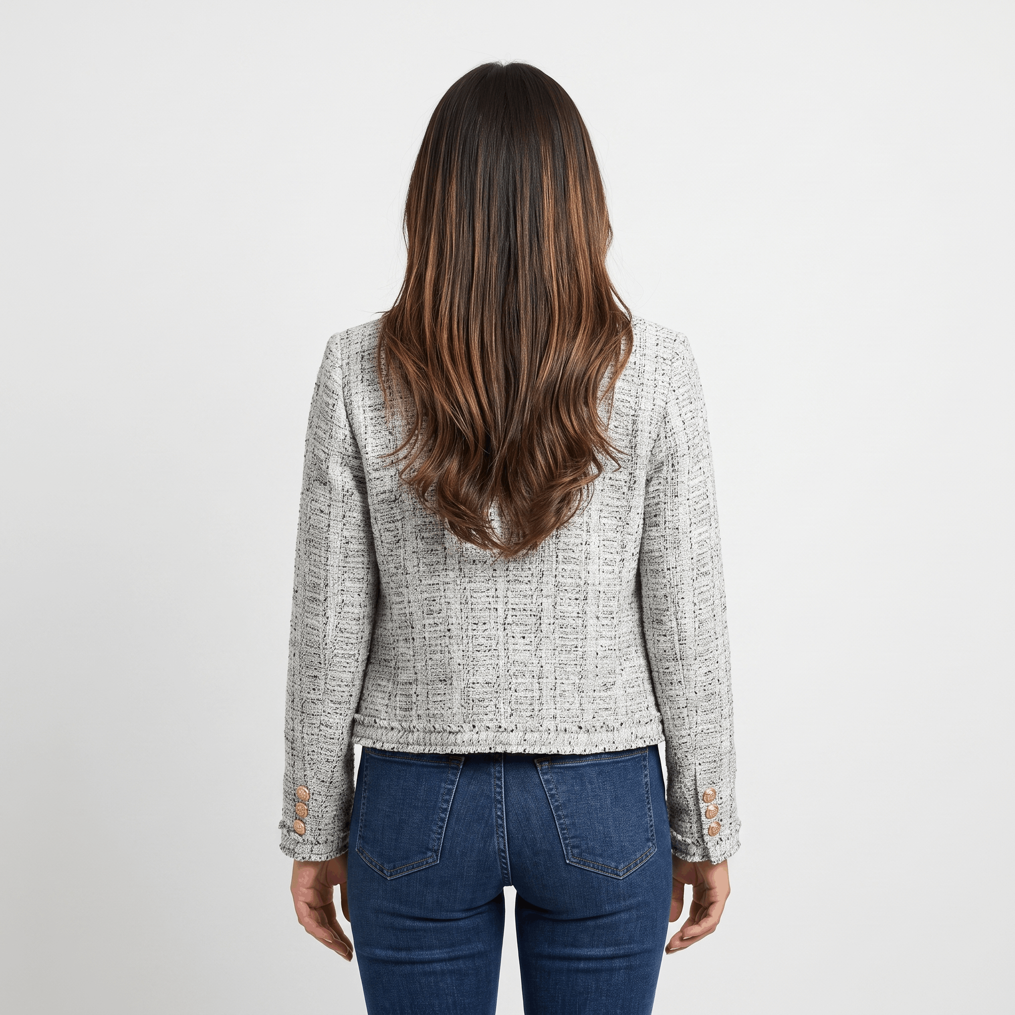 Back view of a woman wearing a light gray textured tweed jacket with a tailored cropped fit and long sleeves.