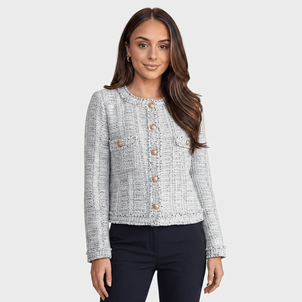 Woman wearing a light gray textured tweed jacket with gold-tone buttons, round neckline, long sleeves, and tailored cropped silhouette, paired with dark trousers.