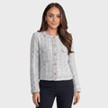 Woman wearing a light gray textured tweed jacket with gold-tone buttons, round neckline, long sleeves, and tailored cropped silhouette, paired with dark trousers.