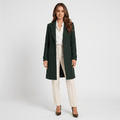 Woman wearing a dark green long coat with a tailored silhouette, notched lapels, button closure, and long sleeves over a white blouse and cream trousers.