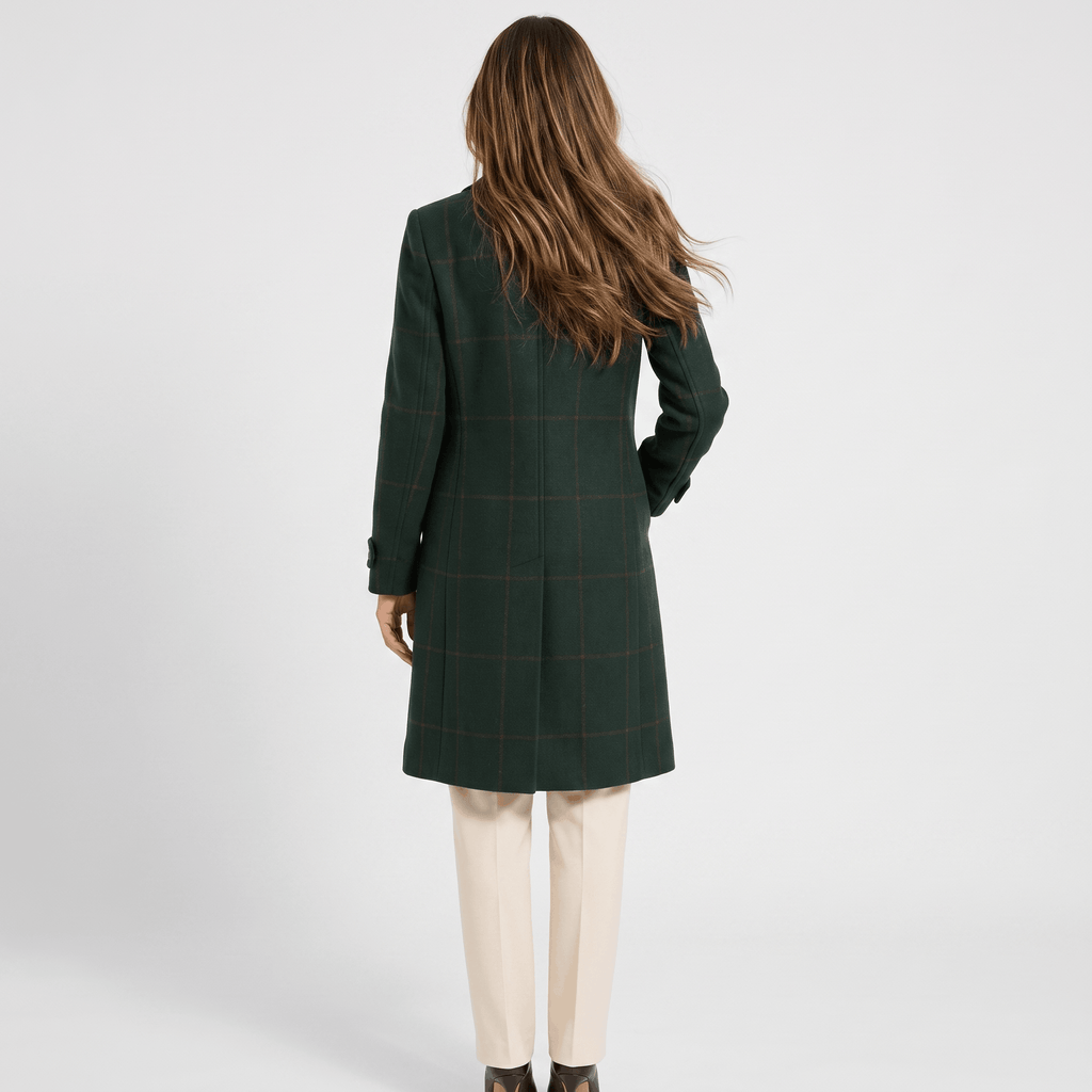 Back view of a woman wearing a dark green tailored long coat with long sleeves and a structured silhouette.