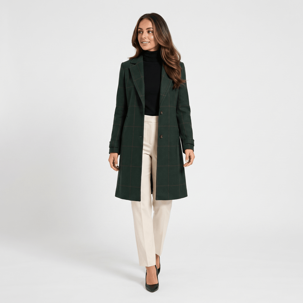 Woman wearing a dark green long coat over a white blouse and cream trousers, shown in a full-body studio view.