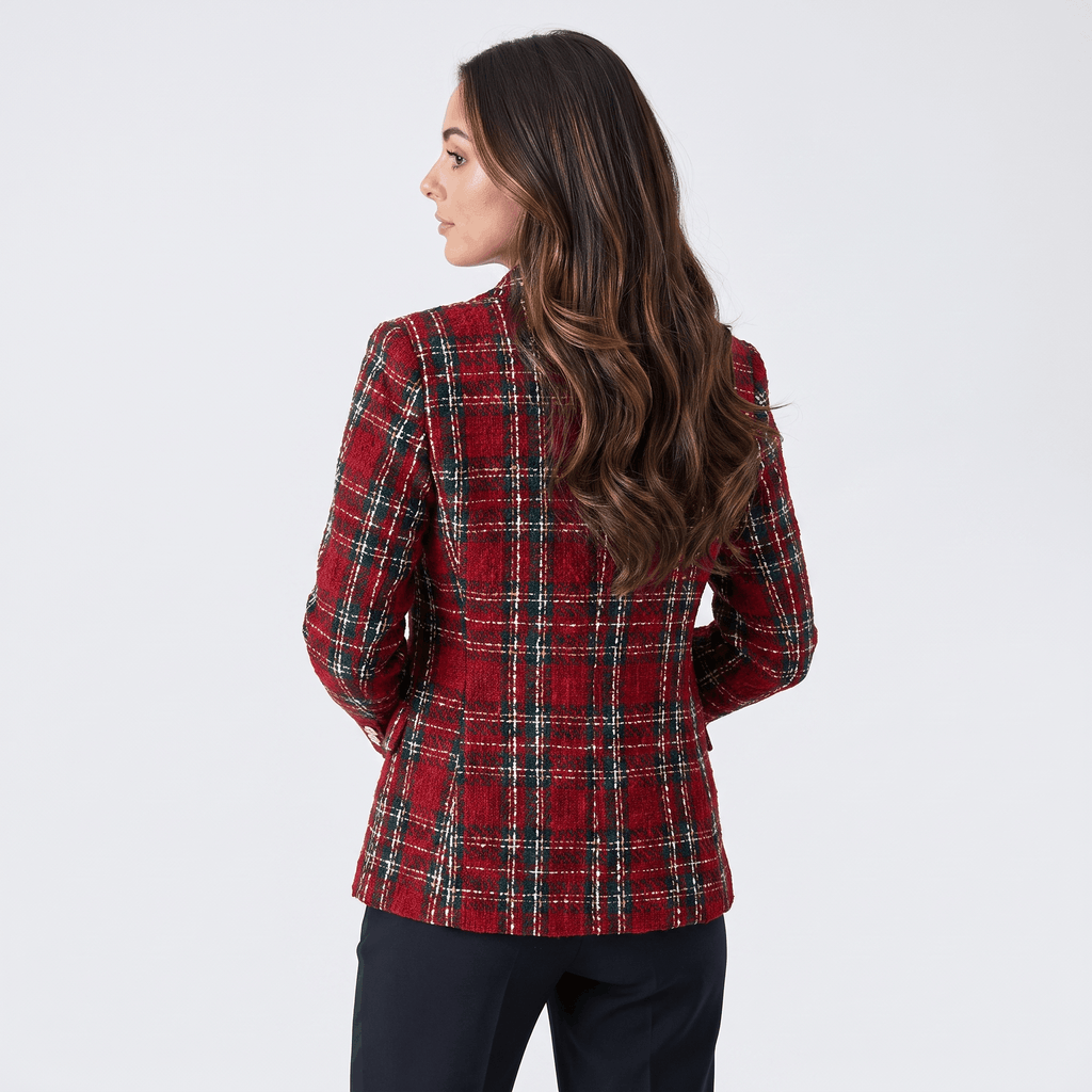 Woman wearing a dark green plaid tweed blazer with dark trousers and ankle boots while walking through a bright modern hallway.