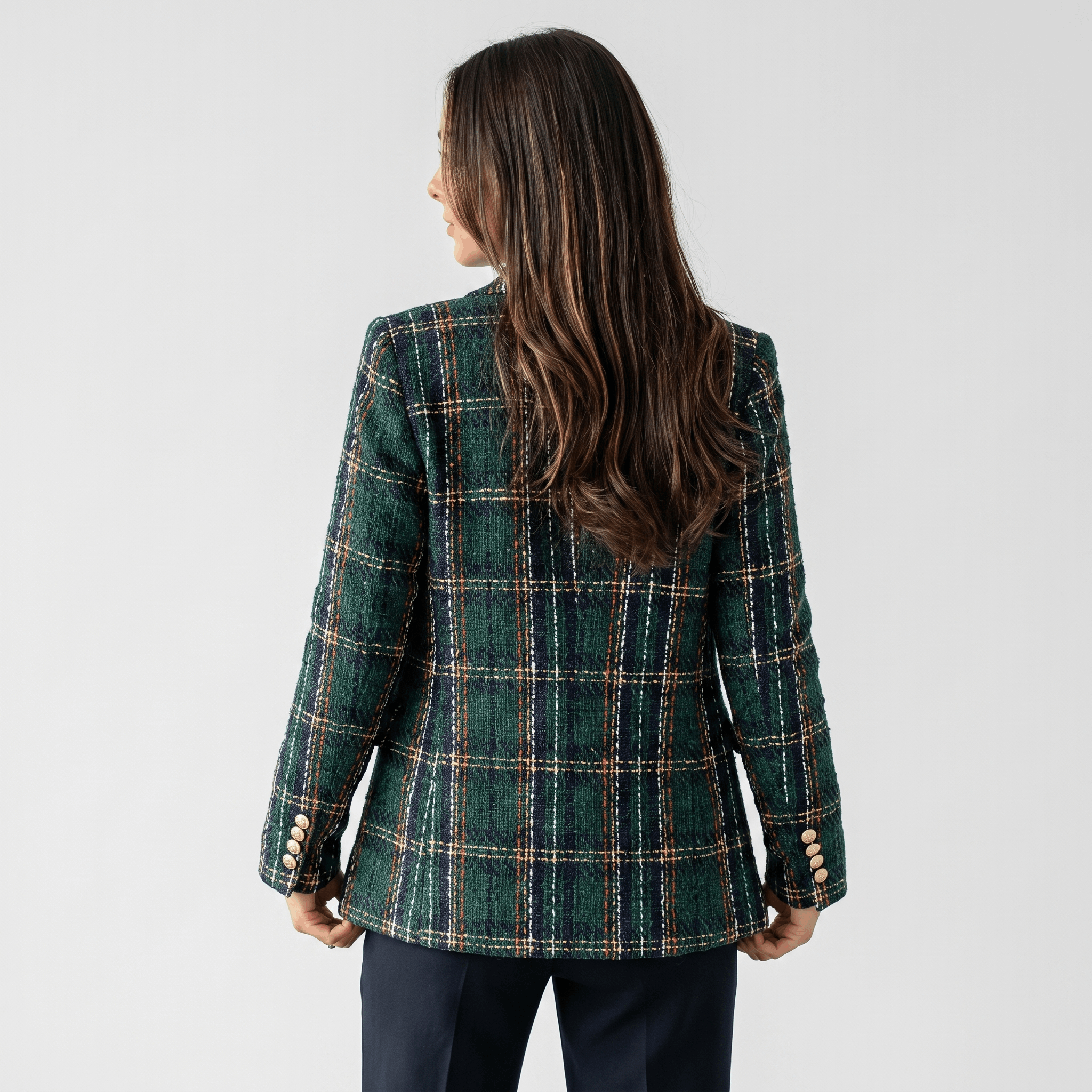 Back view of a woman wearing a dark green plaid tweed blazer with a tailored silhouette and long sleeves.