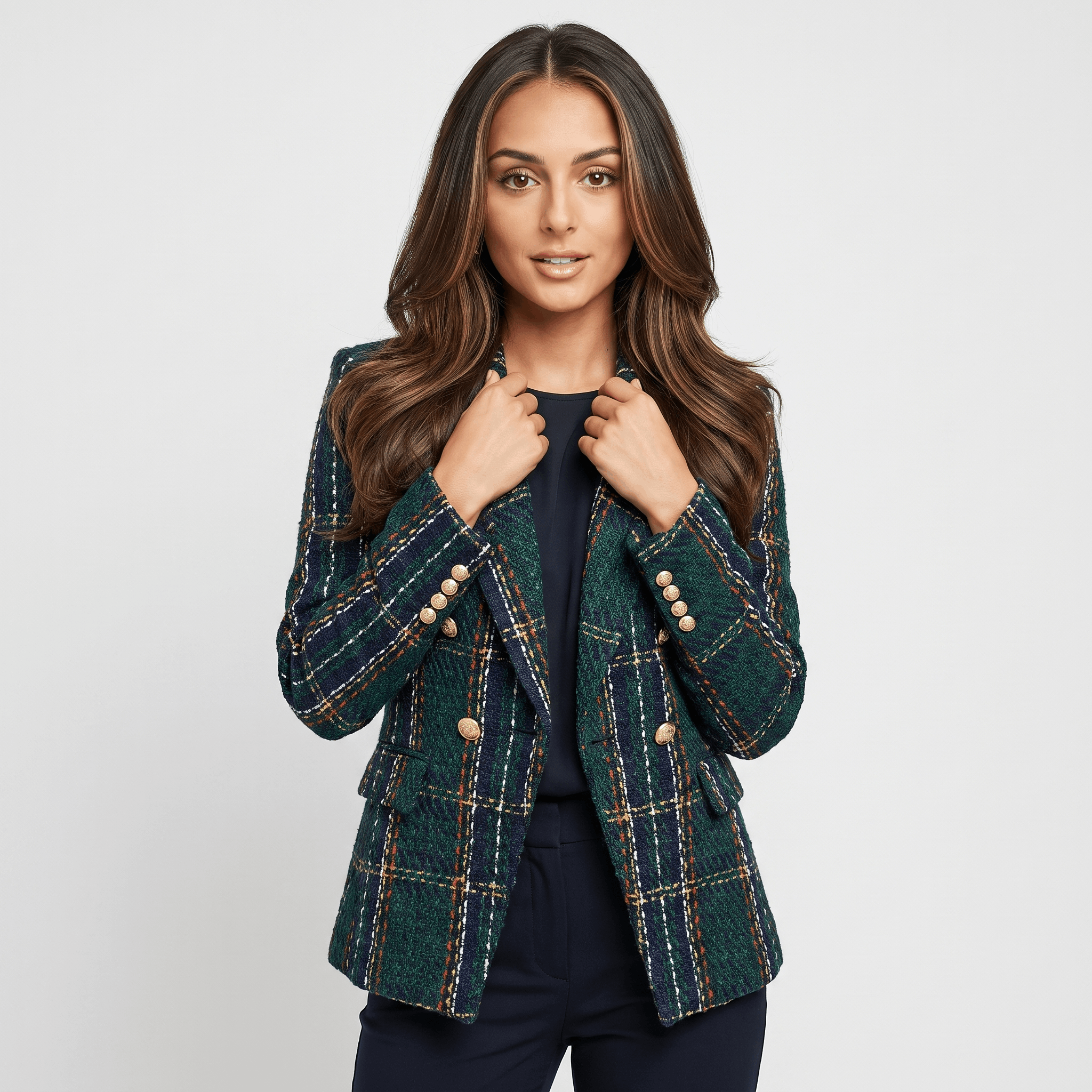 Woman wearing a dark green plaid tweed blazer with gold-tone buttons, notched lapels, and tailored fit over a dark top and trousers.
