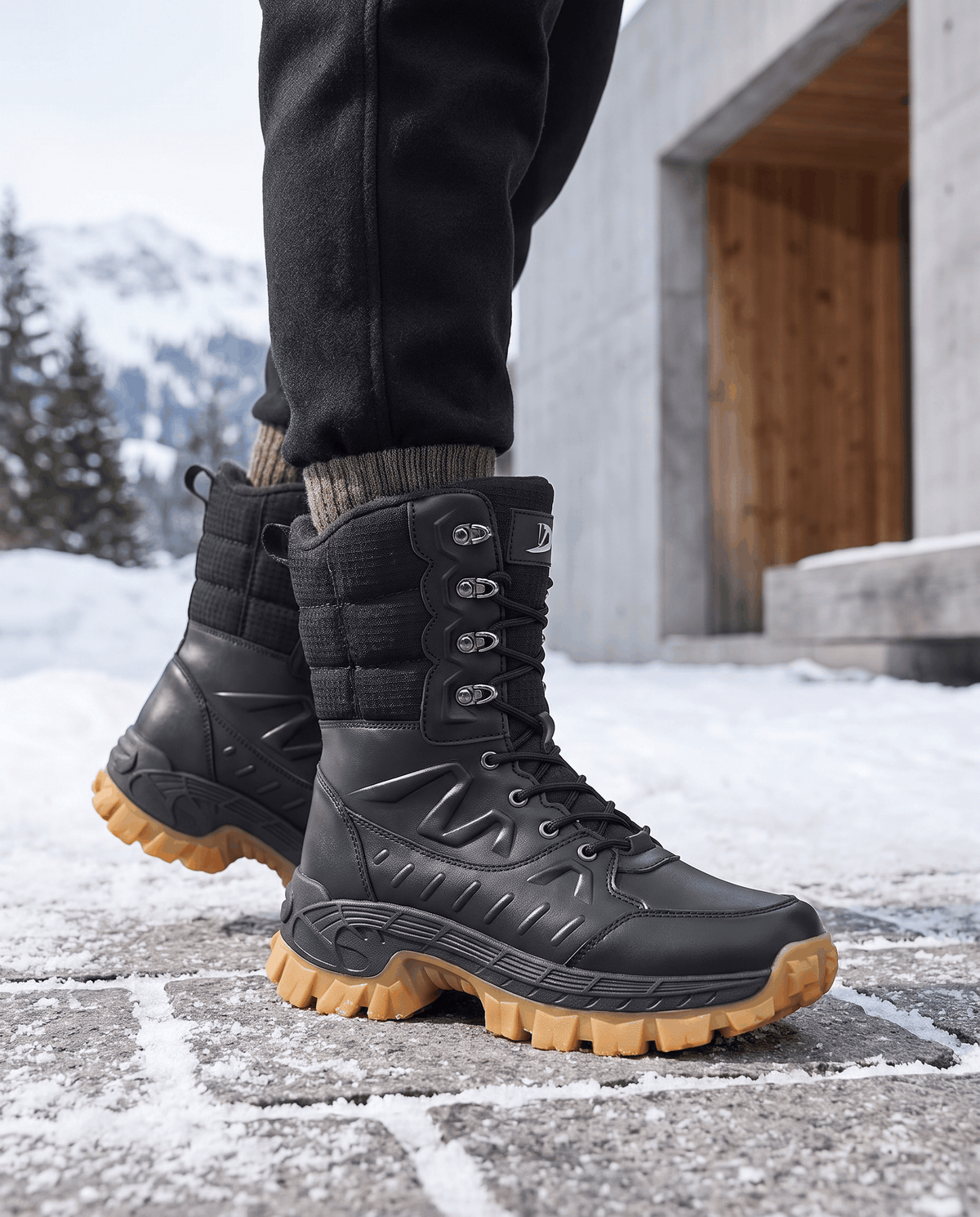 Black lace-up boots with tan soles worn with dark jeans on snowy ground