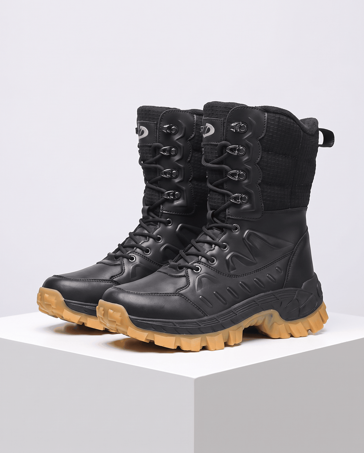 Black lace-up boots with quilted shafts and tan lug soles on a white plinth